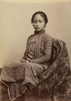 an old black and white photo of a young woman sitting on a chair with a blanket over her head