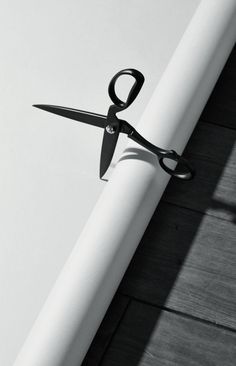 a pair of black scissors sitting on top of a white piece of paper next to a wall