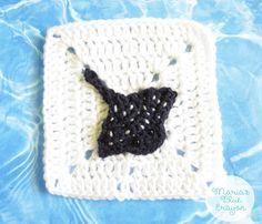 a crocheted square with a black cat on it's side in the water