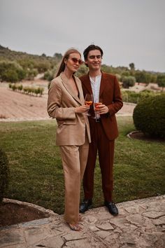 a man and woman standing next to each other holding wine glasses in their hands while posing for the camera