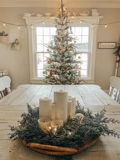 a dining room table with candles on it and a christmas tree in the window behind