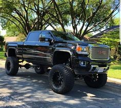 a large black truck parked on the side of a road next to a green tree