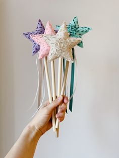 a hand holding up four star shaped hair pins with bows on them, all in pastel colors