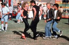 two men and a woman walking in front of an amusement park with people watching them