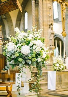 a vase filled with white and green flowers sitting on top of a table in front of a church