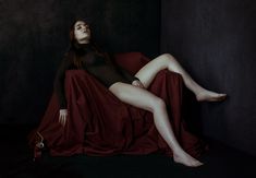 a woman is laying down on a red sheet and posing for the camera with her legs spread out