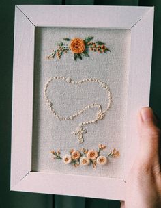 a person holding up a frame with flowers and pearls on the bottom, in front of a green wall