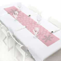 the table is set with white chairs and pink snowflakes on the table runner