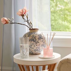 a white table topped with a vase filled with flowers next to a glass cup and reeds