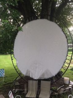 a large white object sitting in the middle of a park next to chairs and trees