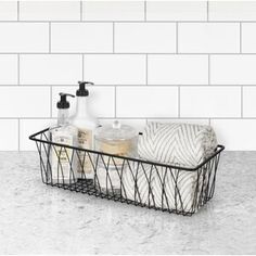 a black wire basket with soap and lotion on the counter in front of a white tiled wall