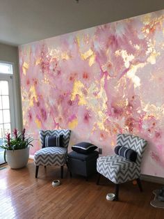 two chairs are sitting in front of a wall with pink and gold paint on it