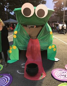 a large green frog float sitting on top of a parking lot next to other colorful plates