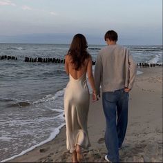 a man and woman walking on the beach holding hands while looking out at the ocean