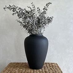 a black vase sitting on top of a wicker table next to a white wall