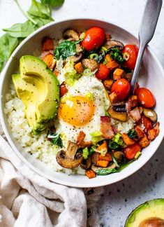 a bowl filled with rice and vegetables next to an avocado on the side