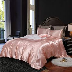 a bed with pink sheets and pillows in a room next to a black wall,