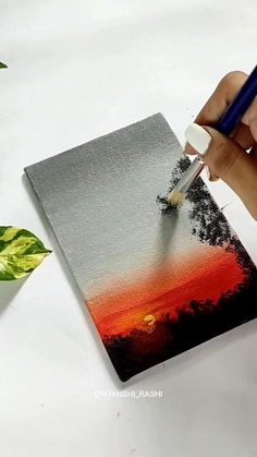 someone is painting an orange and red sunset on a piece of paper with a brush