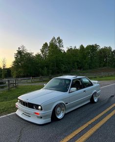 a white car parked on the side of a road next to a field and trees