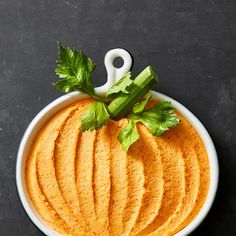 a bowl filled with carrot hummus and celery on top of a table