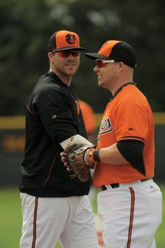 two baseball players standing next to each other on a field with trees in the background