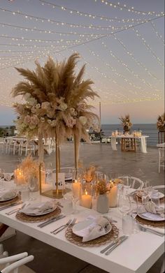 a table set up with place settings and candles for an outdoor dinner by the ocean