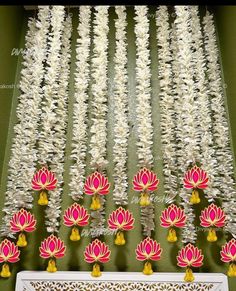 white and pink flowers are hanging from the ceiling in front of a green wall with yellow tassels