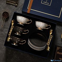 an assortment of gold and silver dishes in a black box on a gray tablecloth