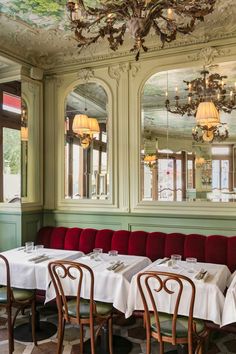 a dining room with tables and chairs, chandelier above the table in front of two windows