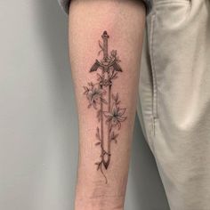 a cross tattoo on the arm with flowers and an arrow is shown in black ink