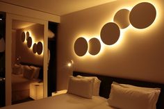 a bed with white sheets and pillows in a room that has round lights on the wall