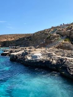 people are swimming in the blue water near some cliffs and stairs on top of them