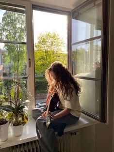 a woman sitting on top of a window sill next to a potted plant