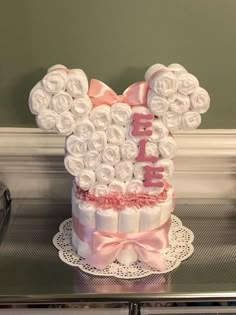 a minnie mouse cake is decorated with white roses and pink ribbon on a doily