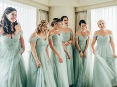 a group of women standing next to each other in front of a window wearing dresses