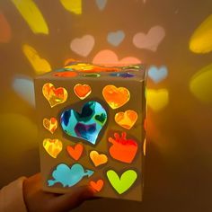 a hand holding up a box with hearts on it and lights in the background behind it