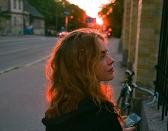 a woman standing next to a bike on the side of a road at sunset or sunrise