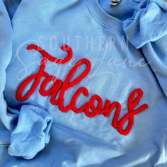 Pullover embroidered with cursive chenille The word Falcons with your team colors. Chenille Color Options: White, Black, Crimson, Maroon, Royal, Navy, Sage, Olive, Pine, Gray, Pale Blue, Aqua Blue, Teal, Mushroom, Bright Yellow, Yellow Gold, Cream, Coral Orange, Neon Orange, Purple. Please message us for custom colors or with any questions. *We use only the highest quality Gildan Heavy Blend Unisex Sweatshirts Varsity T-shirt With Embroidered Graphics For Fall, Collegiate Long Sleeve T-shirt With Letter Embroidery, College Cotton Sweater With Embroidered Graphics, Cotton College Sweater With Embroidered Graphics, Collegiate Tops With Embroidered Graphics For College, Crew Neck T-shirt With Letter Embroidery For College, Collegiate College Tops With Embroidered Logo, Collegiate Tops With Embroidered Logo For College, Varsity Long Sleeve T-shirt With Embroidered Logo