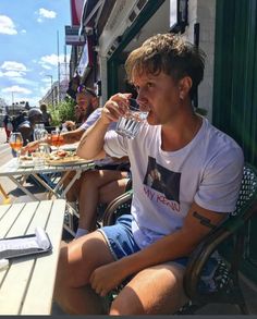 a man sitting at an outdoor table drinking from a wine glass in front of him