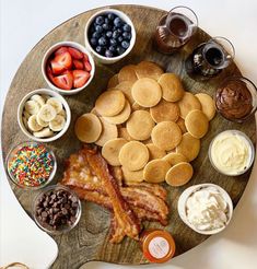 pancakes, bacon, and other breakfast foods are arranged on a wooden platter