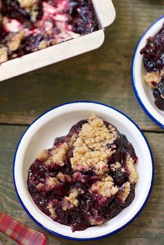 two bowls filled with blueberry crumbles on top of a wooden table