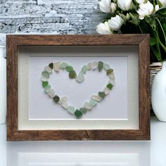 a heart made out of sea glass sitting in a wooden frame next to white flowers