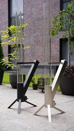 two metal sculptures sitting on top of a cement floor next to plants and potted trees