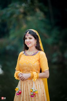 a woman in a yellow dress standing next to a body of water with trees behind her