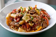 a white bowl filled with pasta and meat on top of a green tablecloth next to a window