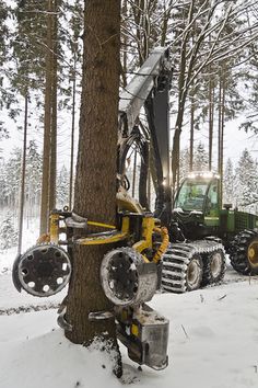 a tractor is parked next to a tree in the snow with other equipment around it