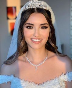 a woman in a wedding dress wearing a tiara and smiling at the camera with her veil draped over her head