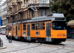 an orange trolly car is on the tracks in front of some buildings and people