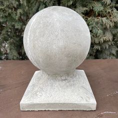 a large white stone ball sitting on top of a wooden table next to a tree