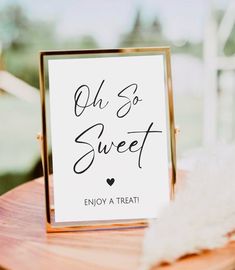 a sign that says oh so sweet on top of a wooden table next to a white feather